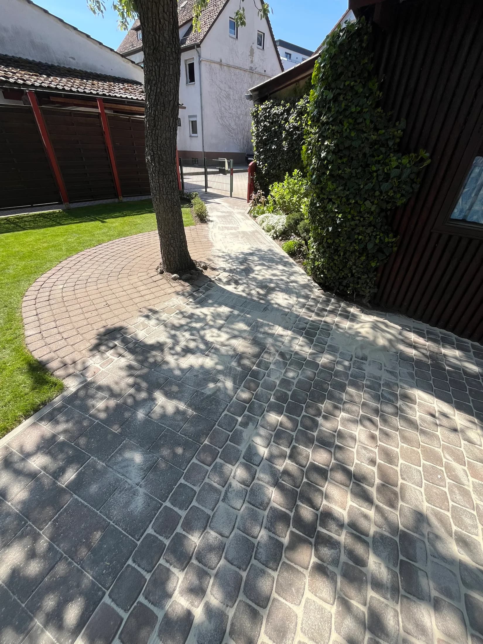 Geschwungener Pflasterweg neben einer Rasenfläche und einem Gartenhaus