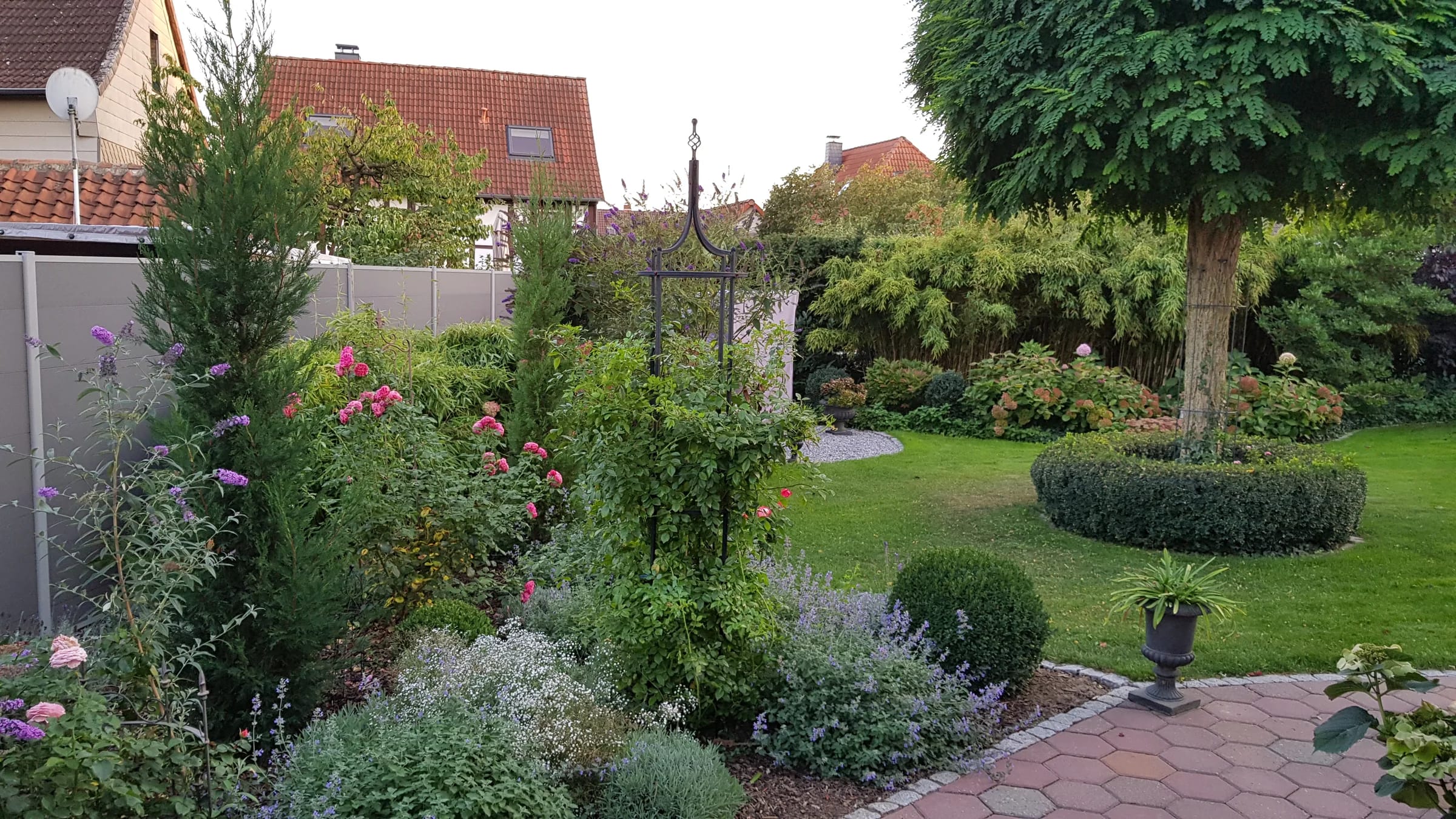 Ein von Frank John gestalteter Garten mit blühenden Beeten, Rasen und gepflastertem Gartenweg